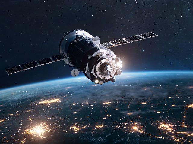 Ein Satellit in der Erumlaufbahn. Im Hintergrund die Erde bei Nacht