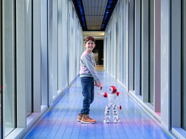 Ein Junge hält einen NAO-Roboter an der Hand